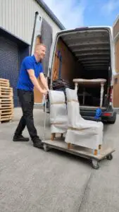 Man and van transporting wrapped appliance on heavy-duty trolley.