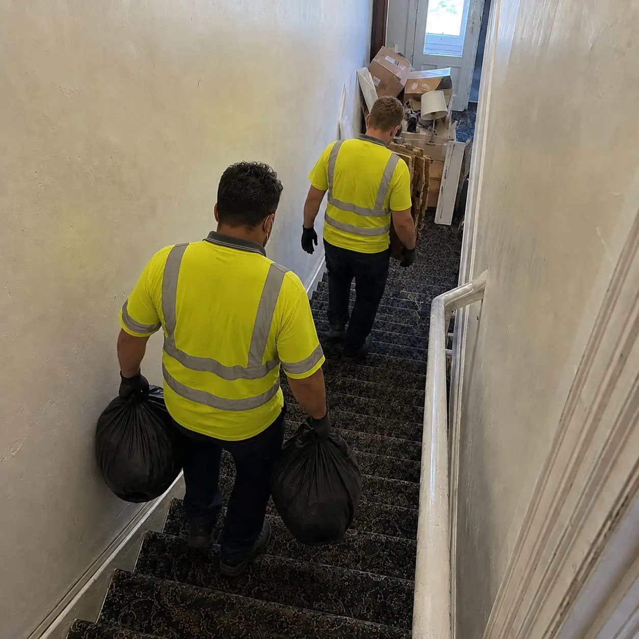 Flat clearance workers carrying rubbish bags down a narrow staircase