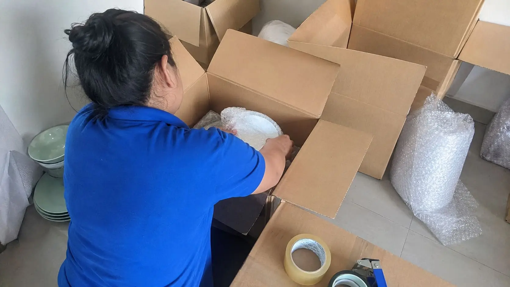 Professional packer carefully wrapping household items beside open moving boxes