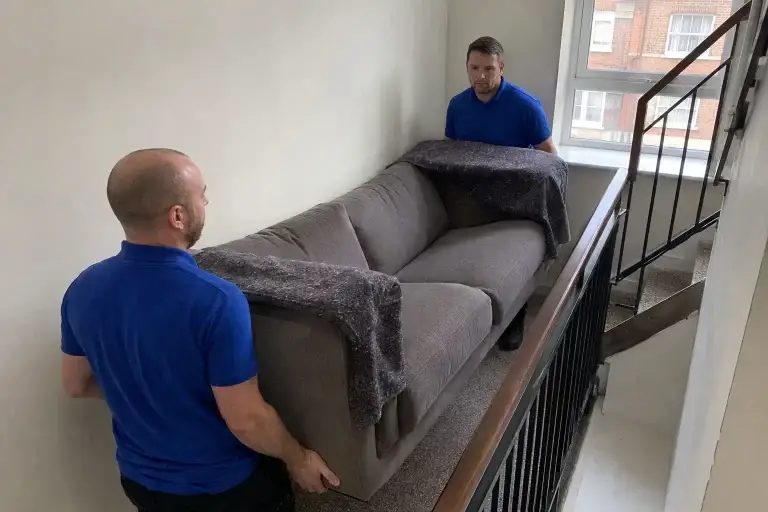 Royal blue removal men carrying sofa upstairs in London flats - Illustrative Image