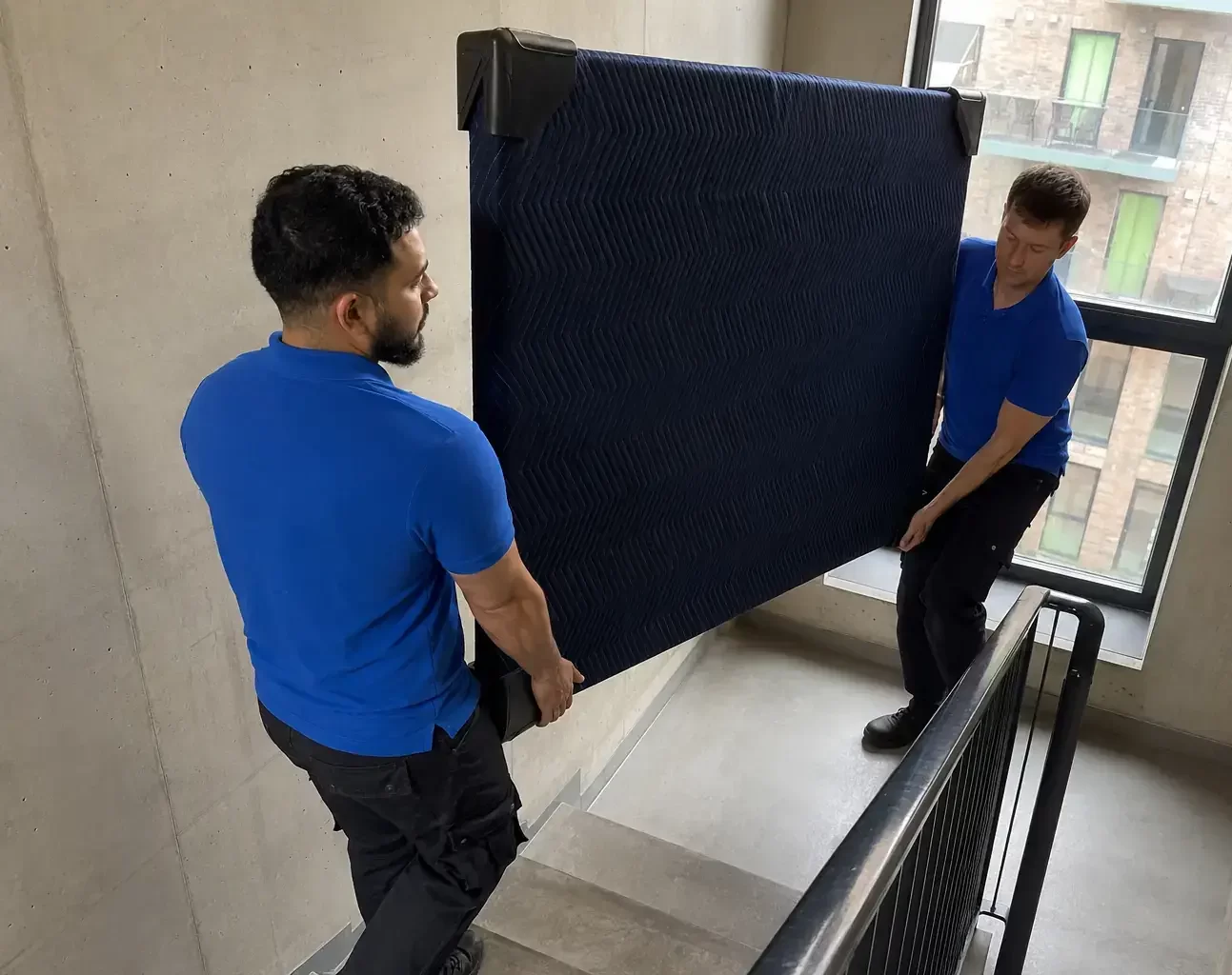 Two removal men moving protected mirror upstairs in flats